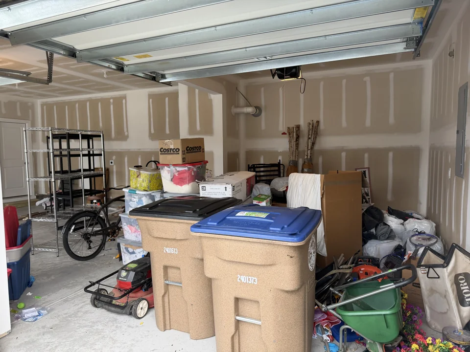 Storage bins, yard equipment, and belongings clustered behind trash cans before organizing