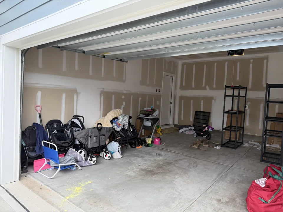 Strollers and belongings along the garage wall before organizing
